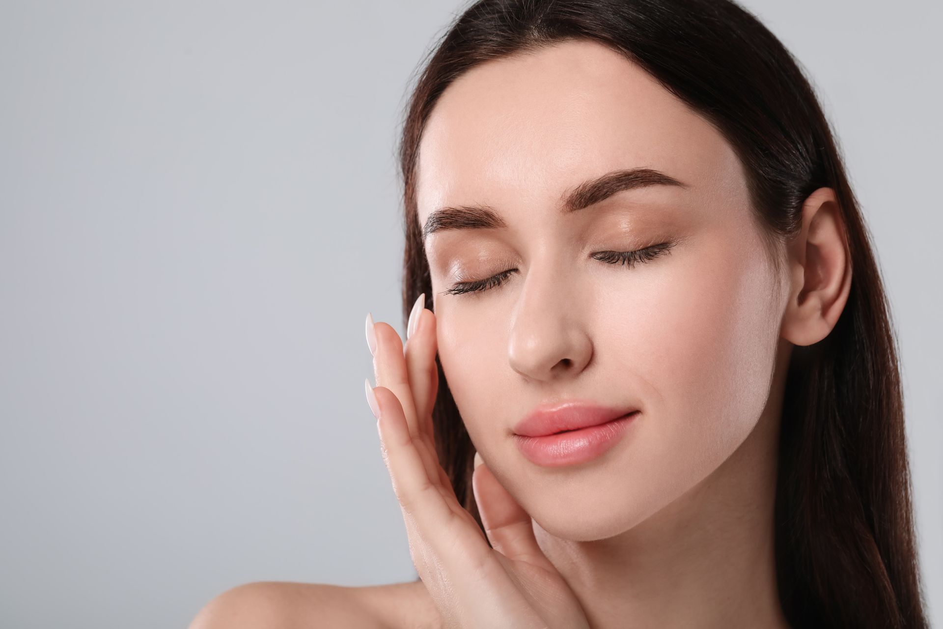 A woman with her eyes closed is touching her face with her hand.