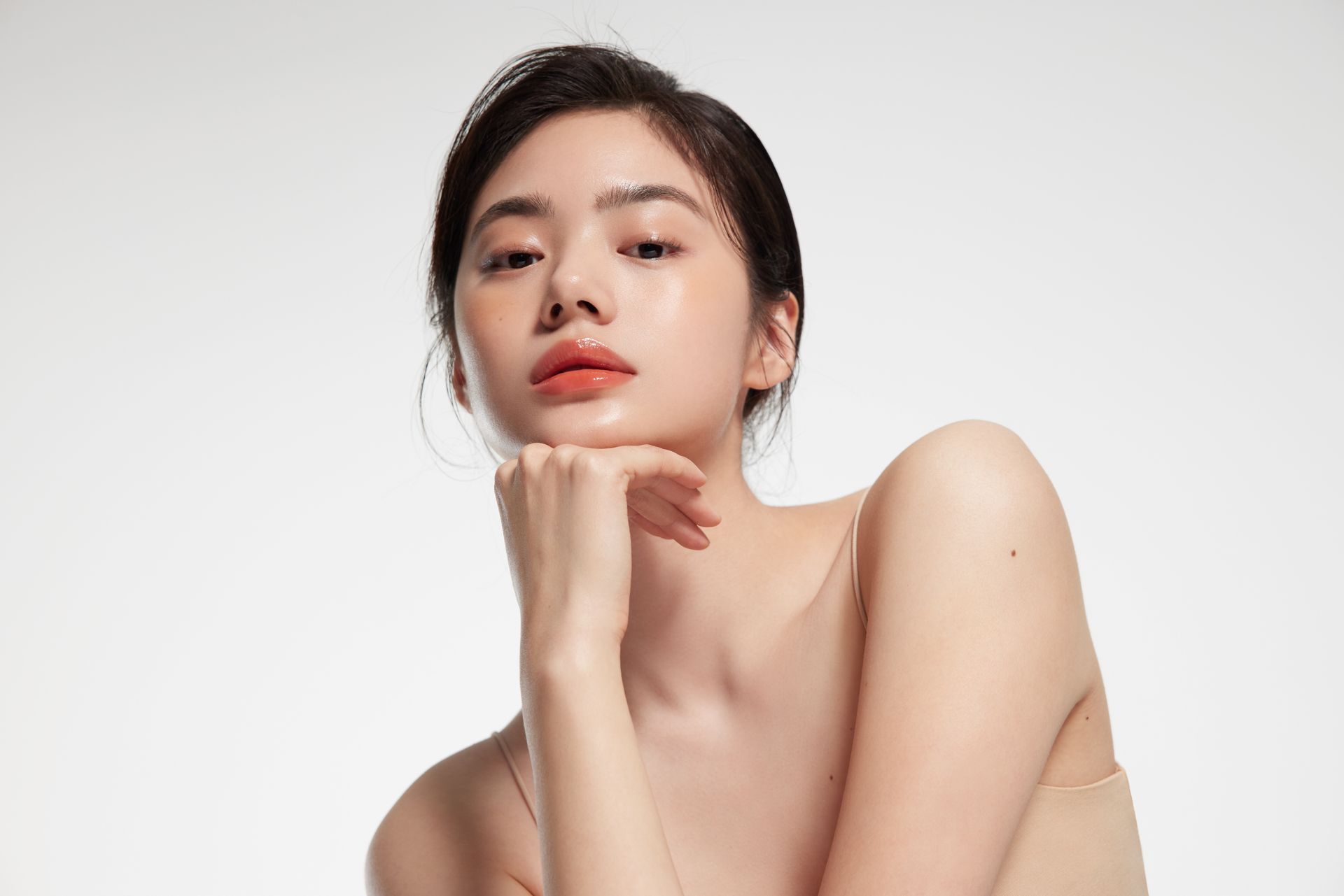 A woman without a shirt is holding her hand to her chin and looking at the camera.