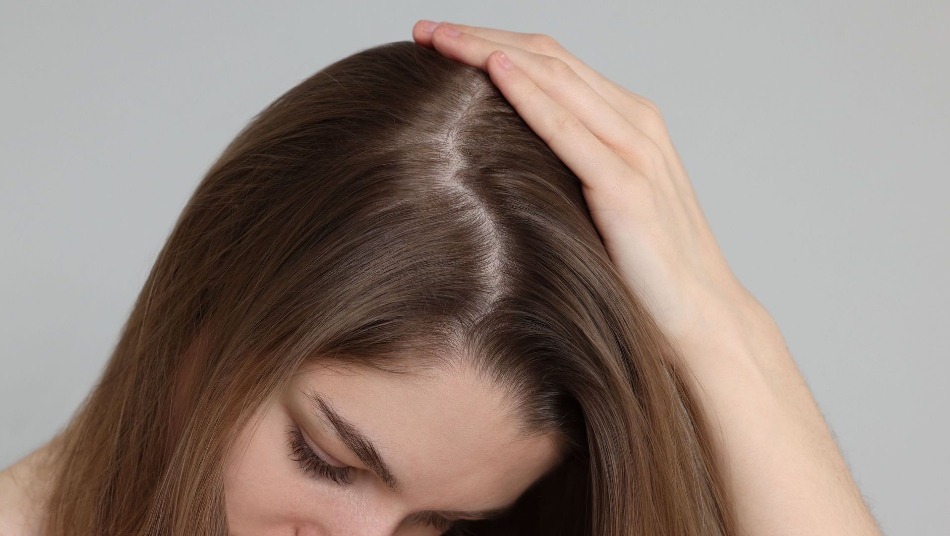 A woman is touching her hair with her hand.