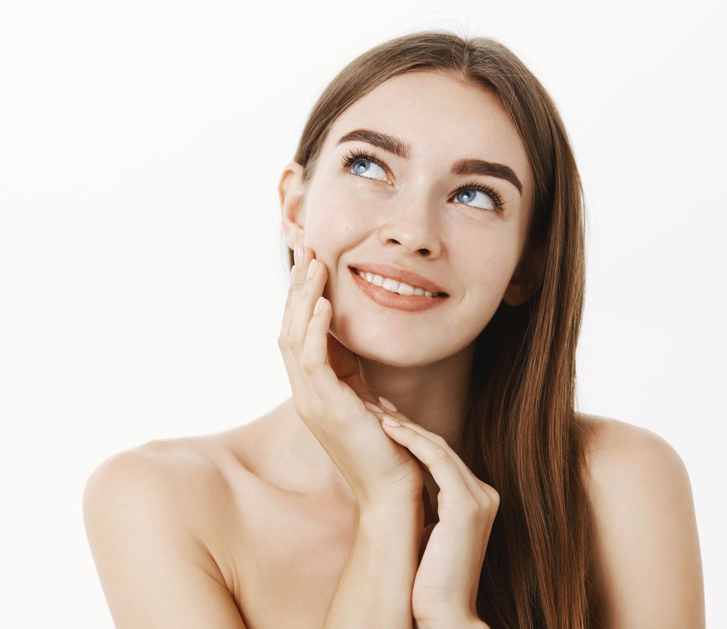 A woman with long hair is smiling and touching her face.