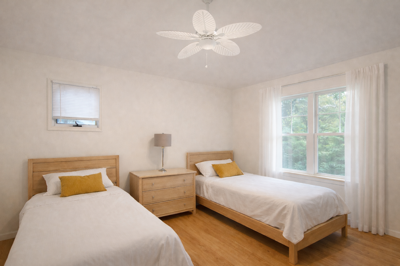 Two beds in a light-filled bedroom with a window, ceiling fan, and wooden furniture.