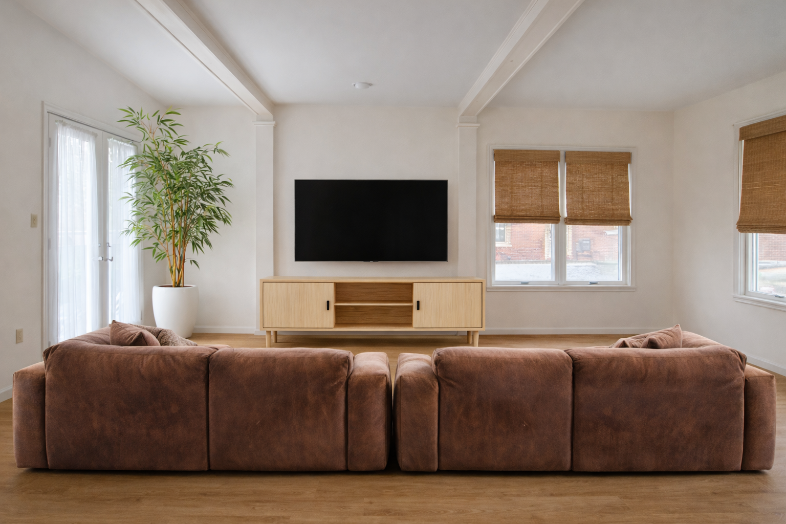 Living room with brown sectional sofa, TV, wooden console, and large plant.