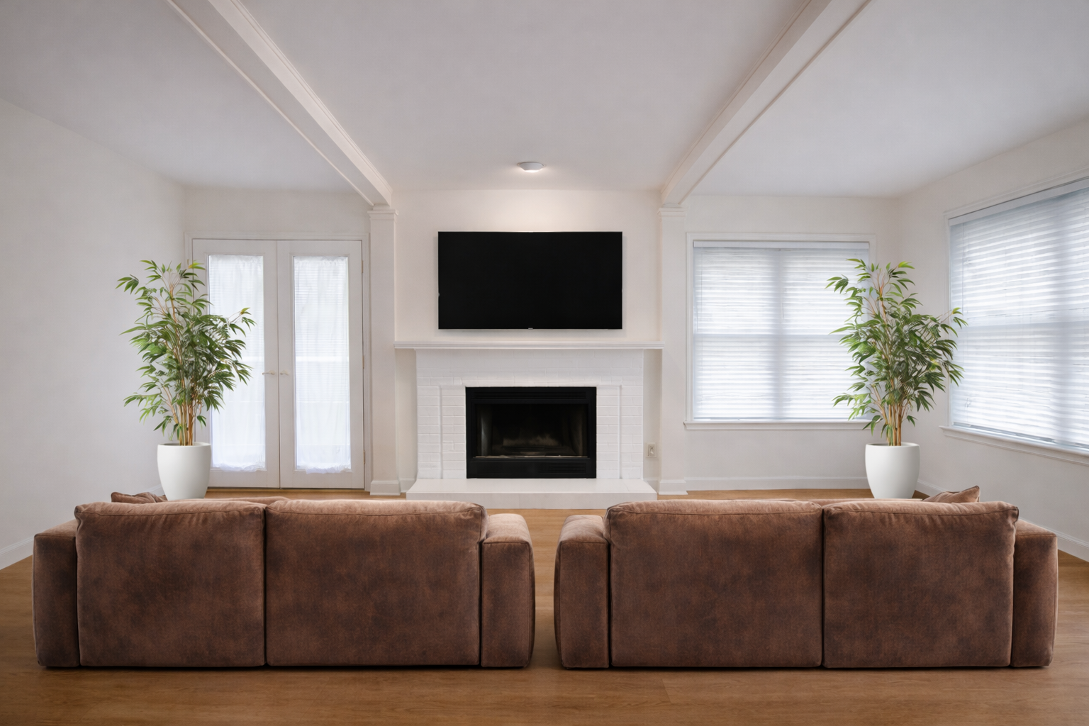Living room with brown sofas facing a fireplace with a mounted TV. Plants flank the sofas and windows.