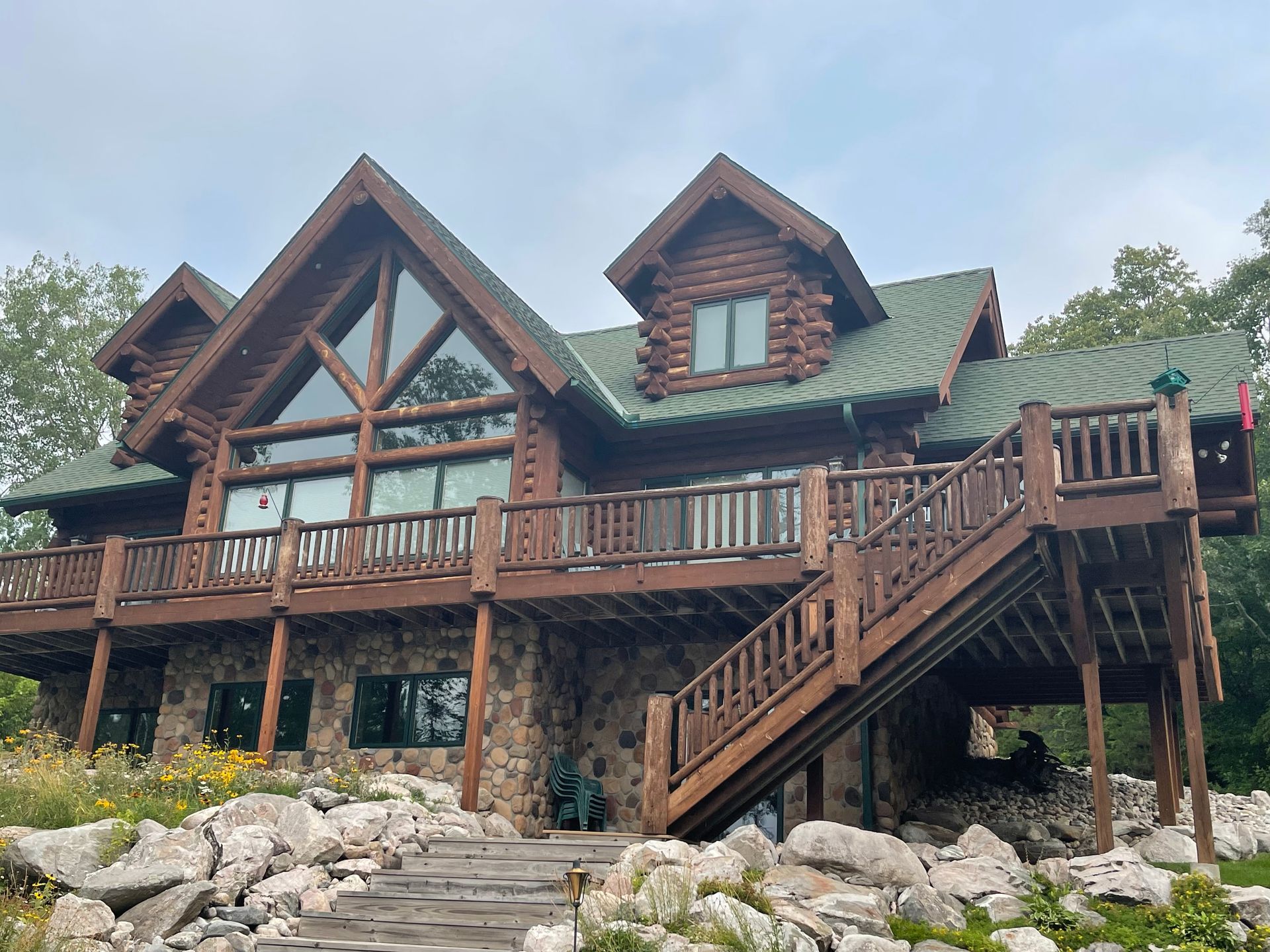 A Large Log Cabin With a Green Roof and Stairs – MN - Lifetime Staining and Log Restoration
