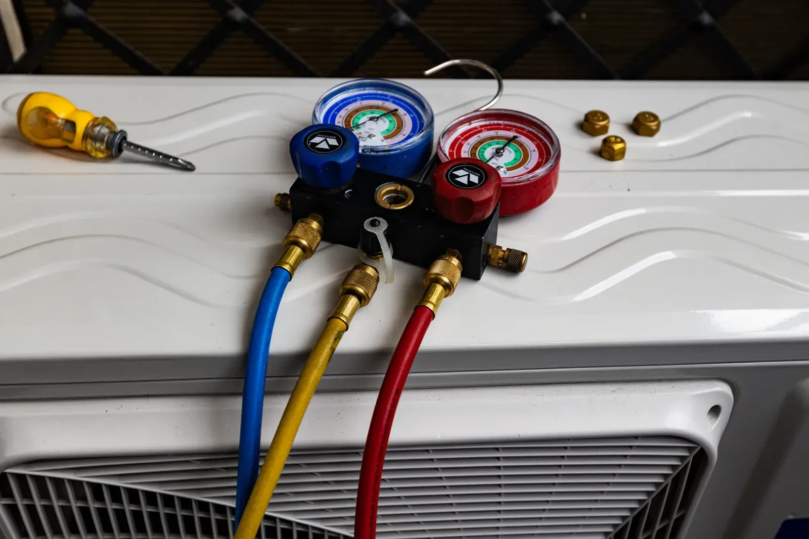 HVAC manifold gauges with blue, yellow, and red hoses connected to an air conditioner unit