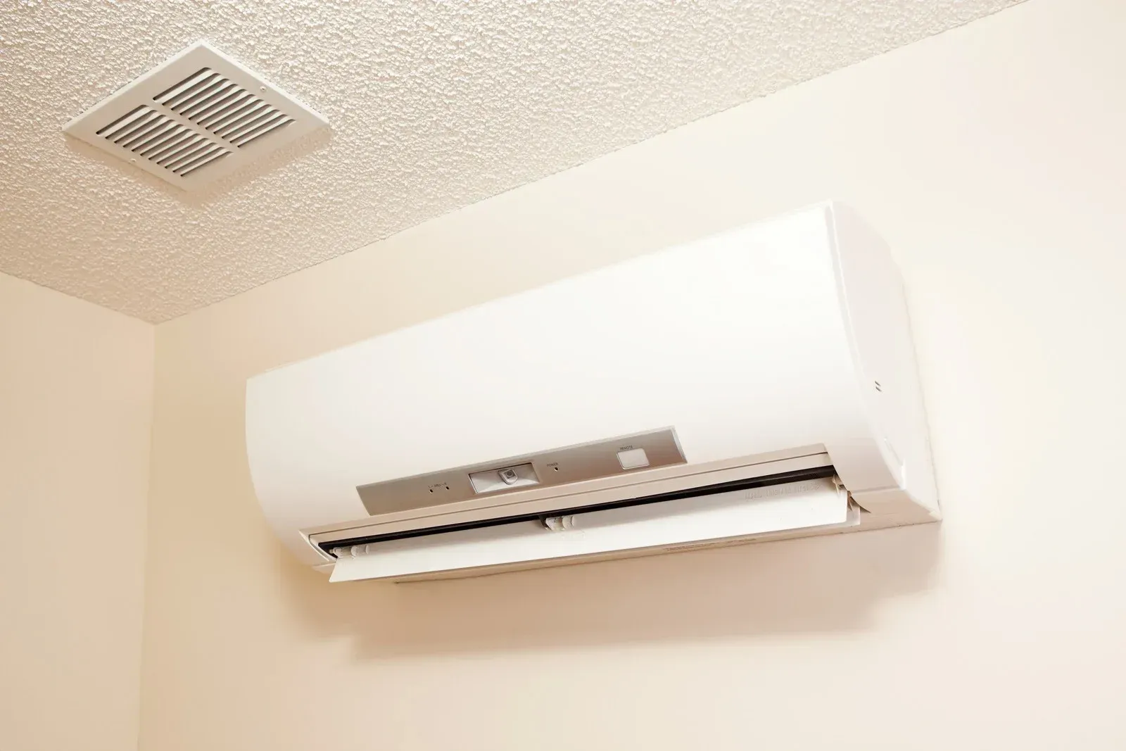 White wall-mounted air conditioner installed near the ceiling in a beige room.