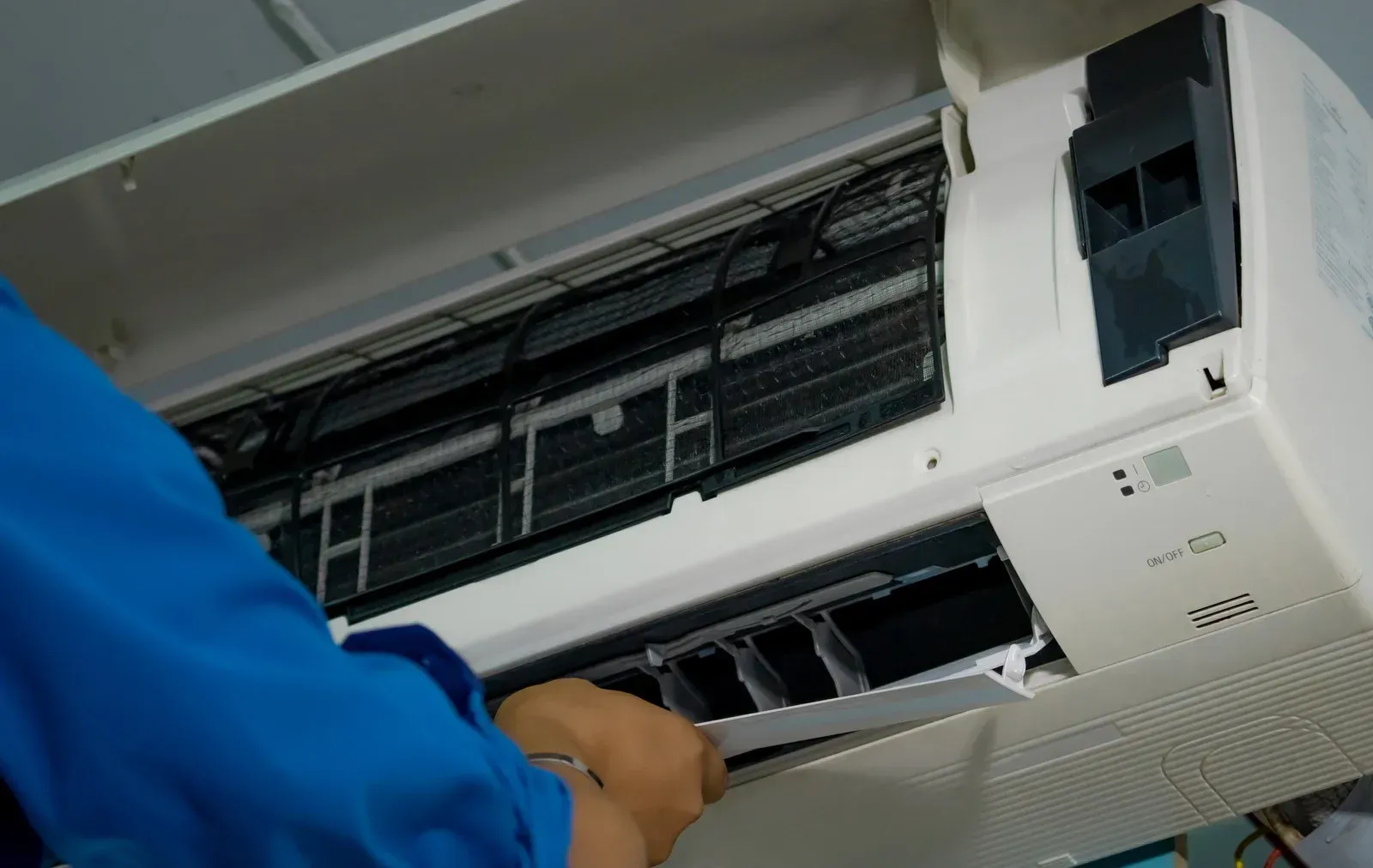 Technician cleaning an open wall-mounted air conditioner filter with a blue sleeve visible