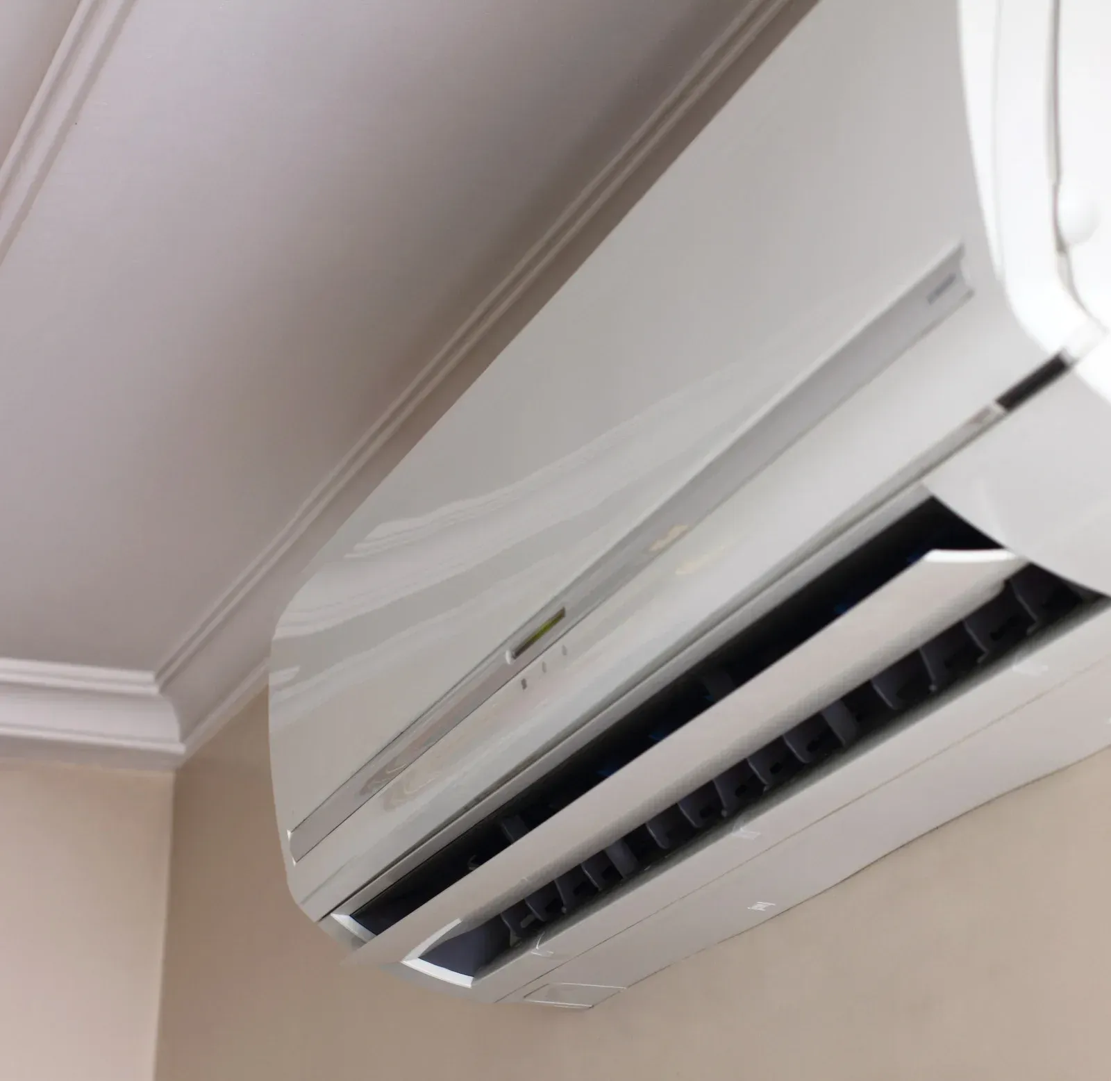 Wall-mounted white air conditioner beneath a ceiling corner, vent open.