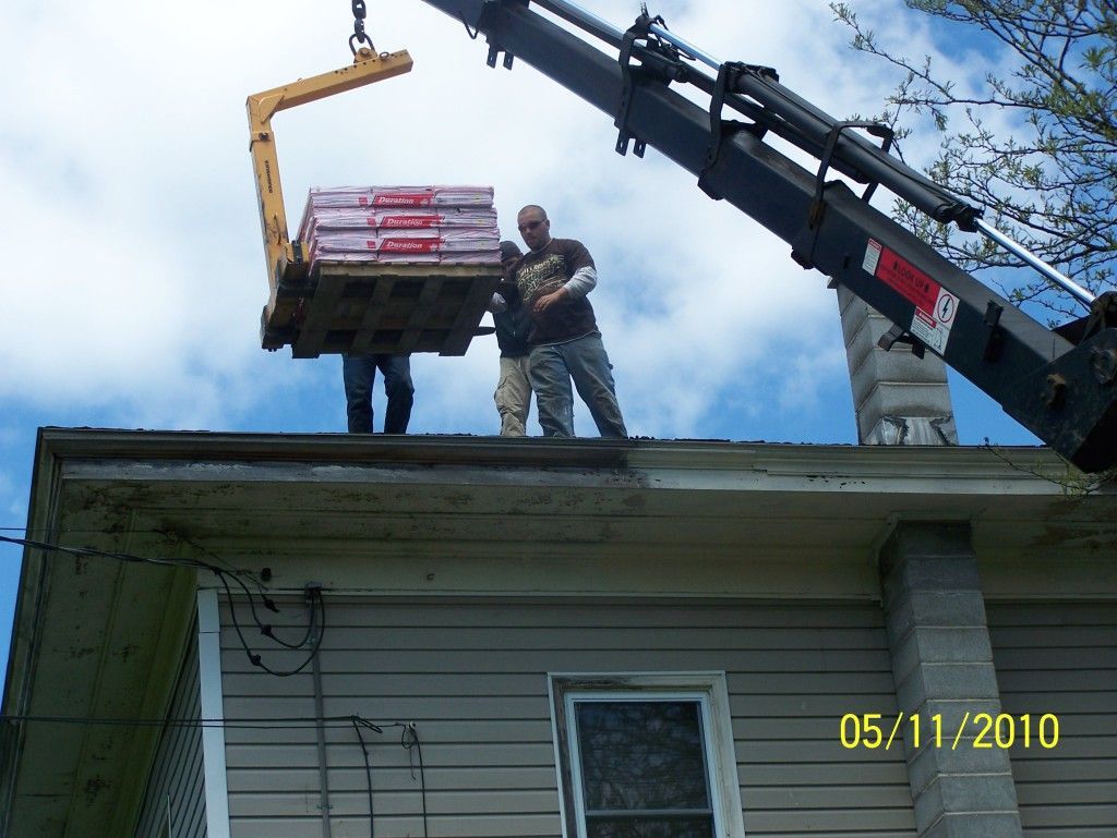 Two men are standing on the roof of a house being lifted by a crane