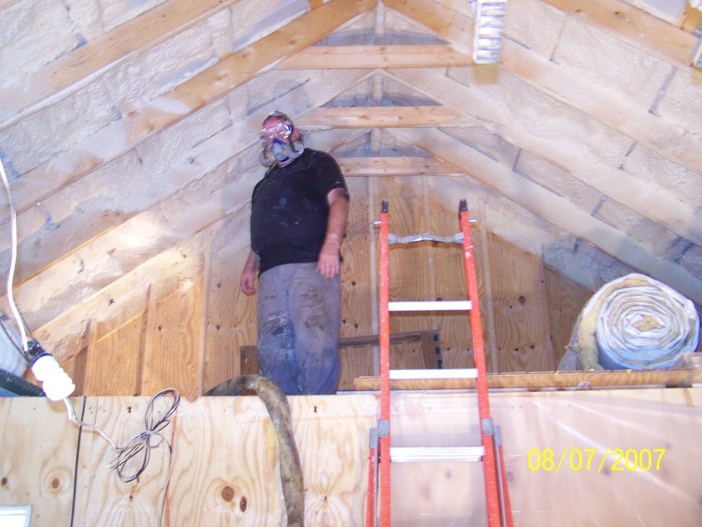 A man is standing on a ladder in an attic.