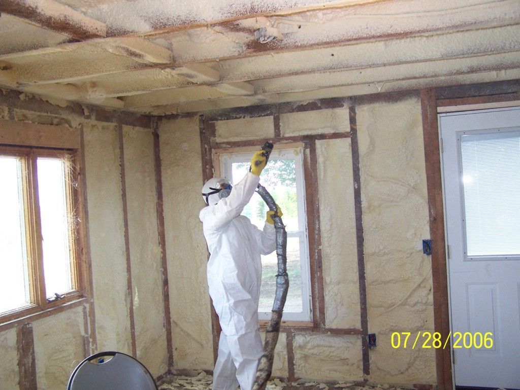 A man in a protective suit is spraying insulation on a wall.