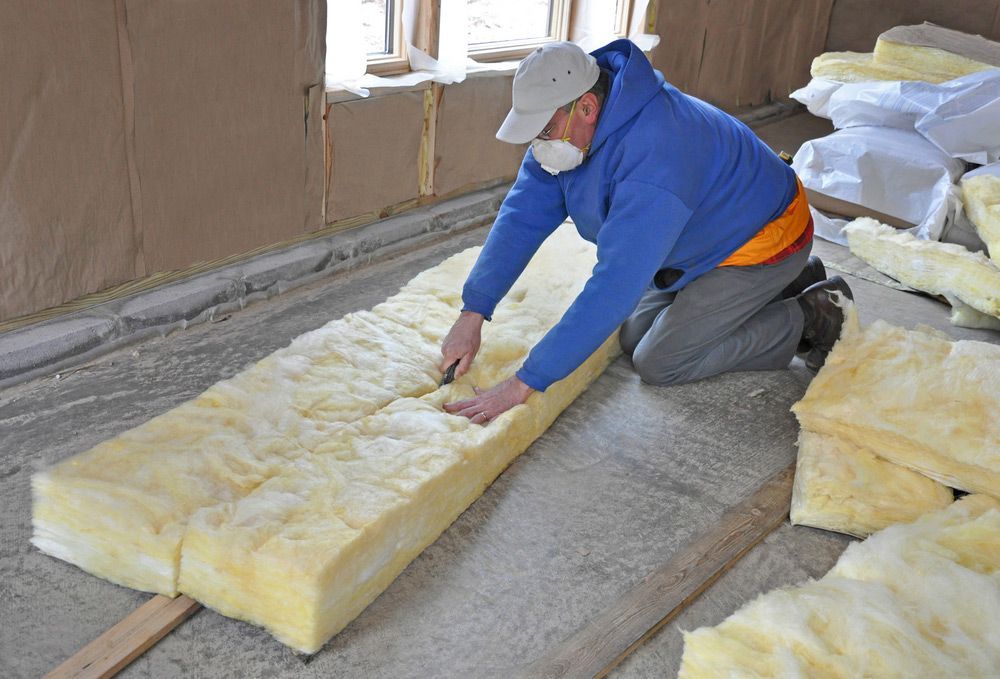 A man is kneeling on the floor cutting a piece of insulation.