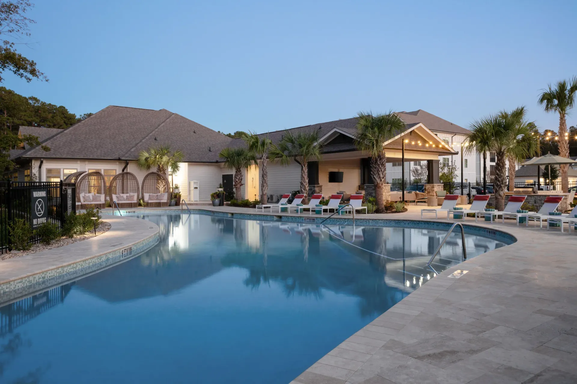 Outdoor community pool with palm trees, cabanas, and lounge chairs.