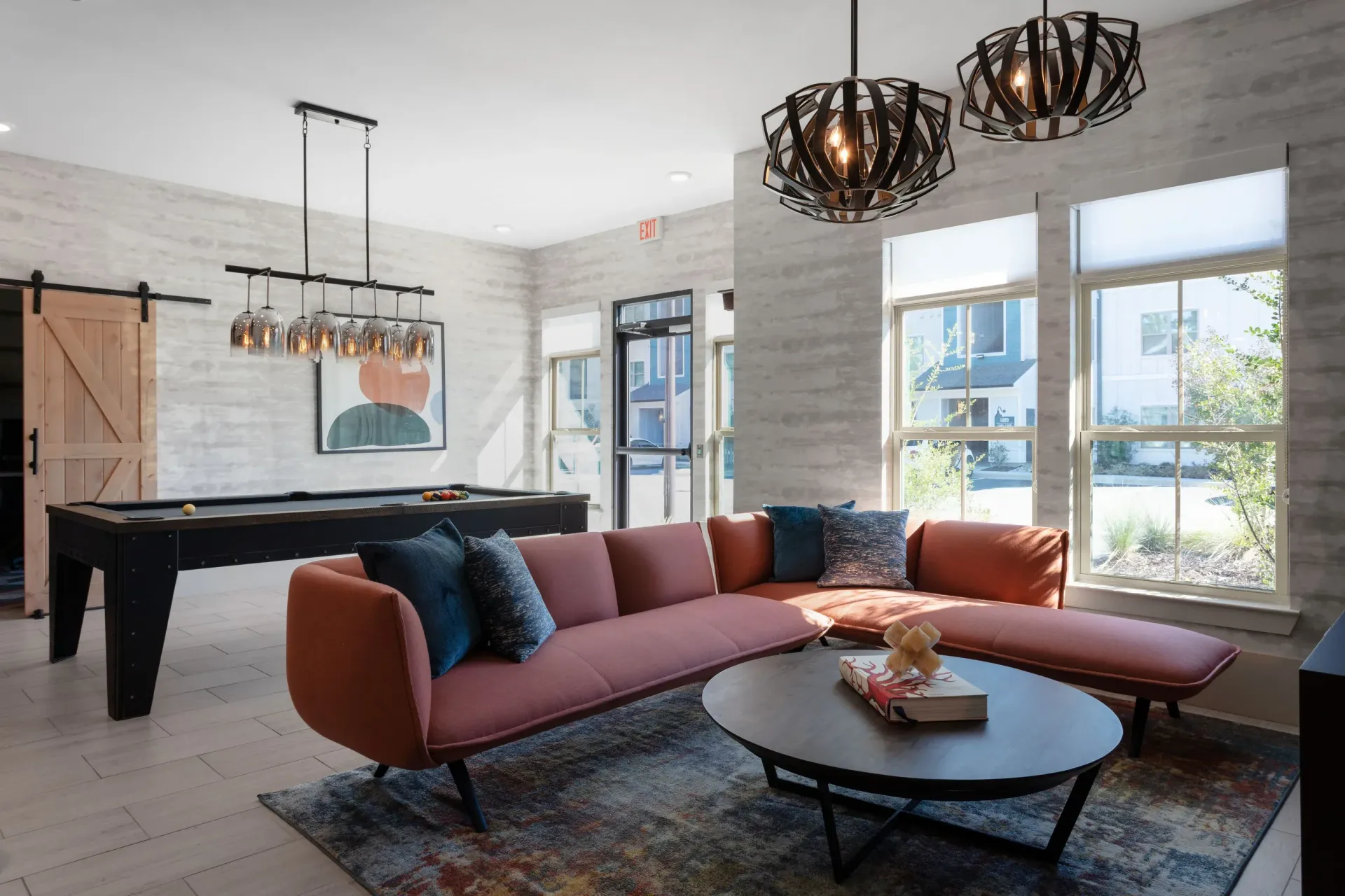 Interior communal lounge with pink sectional sofa, pool table, and large windows