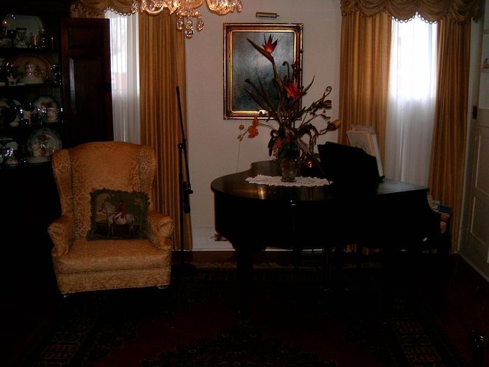 A room with a yellow armchair, piano, floral arrangement, and gold curtains.