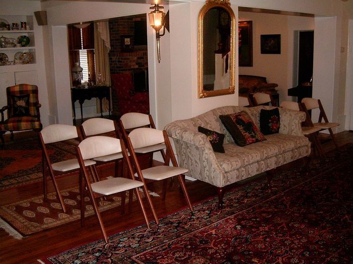 Six folding chairs face a sofa in a room with rugs and a mirror.