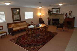 Living room with antique furniture, rug, fireplace, and artwork. Beige walls and carpet.
