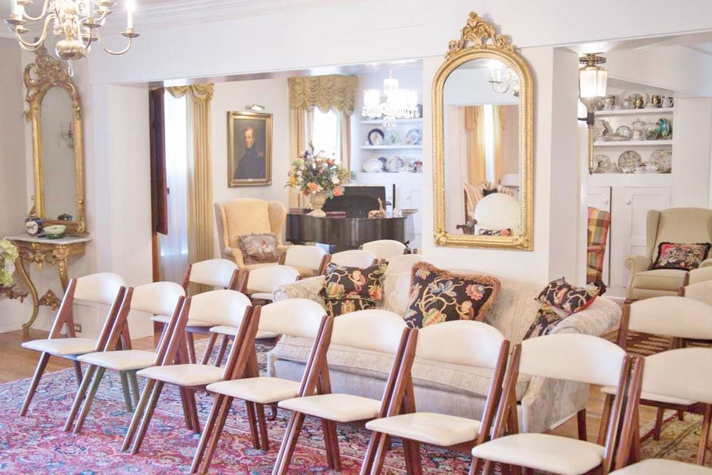 An elegant room set up for a meeting or presentation. Chairs in rows face sofas, mirrors, and a portrait.
