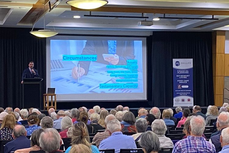 A speaker at a conference addresses a seated audience with a presentation on a screen.