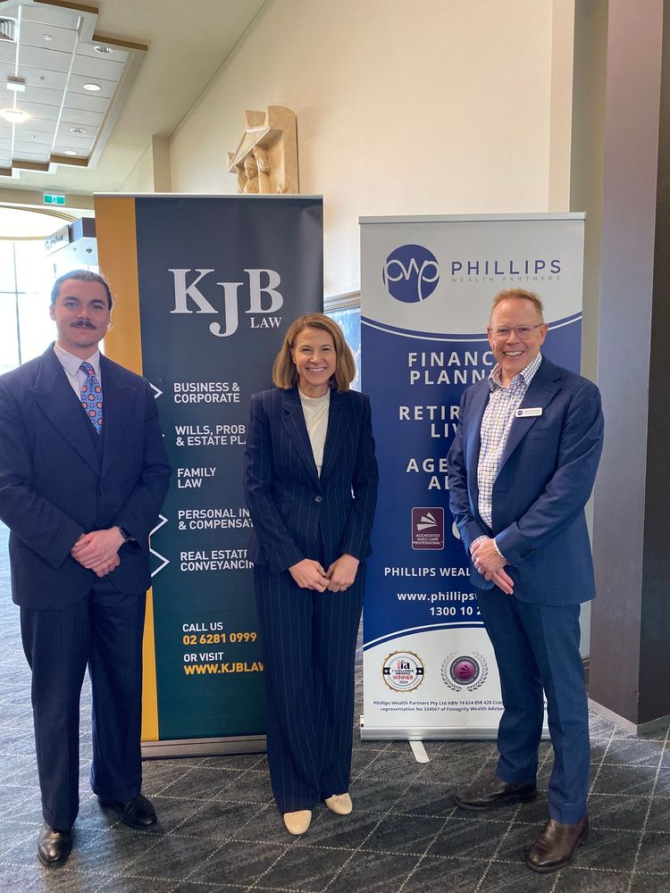 Three people standing by banners at an event, suited in navy and business casual.