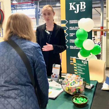 Woman at a booth for KJB Law, speaking with another person. Balloons and marketing materials are visible.
