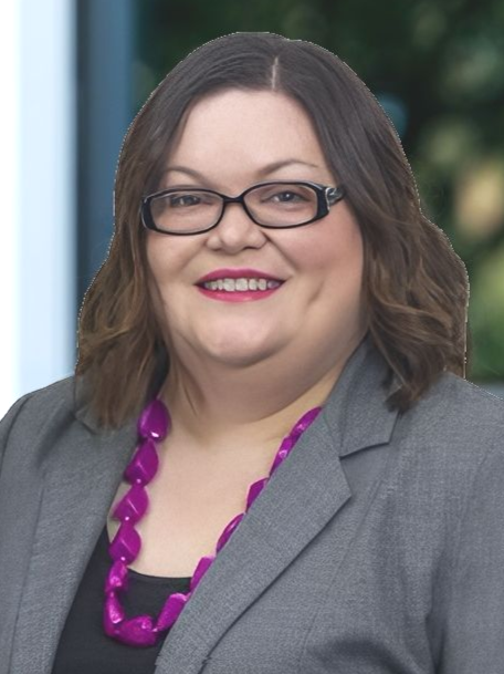Woman with brown hair in front of a building, wearing a blazer and patterned shirt, smiling.