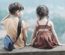 Boy and girl sitting side-by-side on a ledge, looking at the view. Boy in yellow shirt, girl in brown dress.