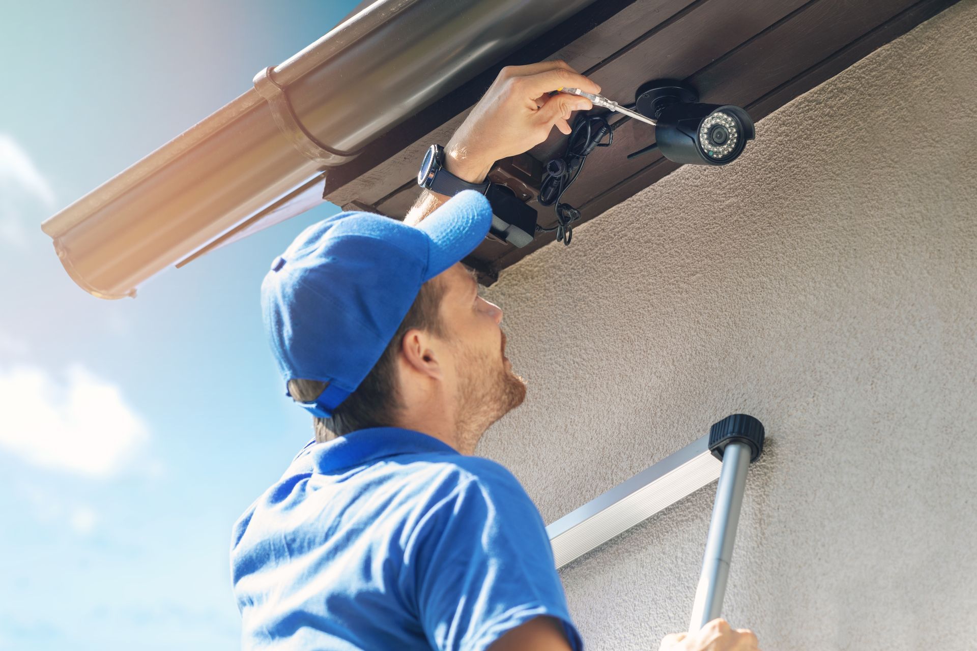 A technician under a roof gutter on a beige exterior wall.