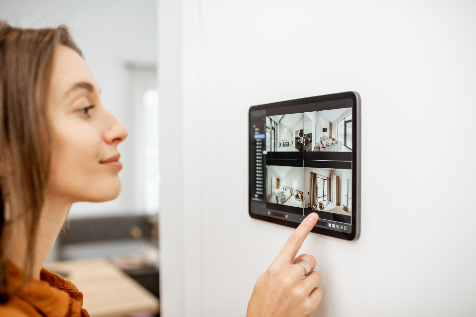 Person using a wall-mounted smart home control panel displaying security camera feeds.
