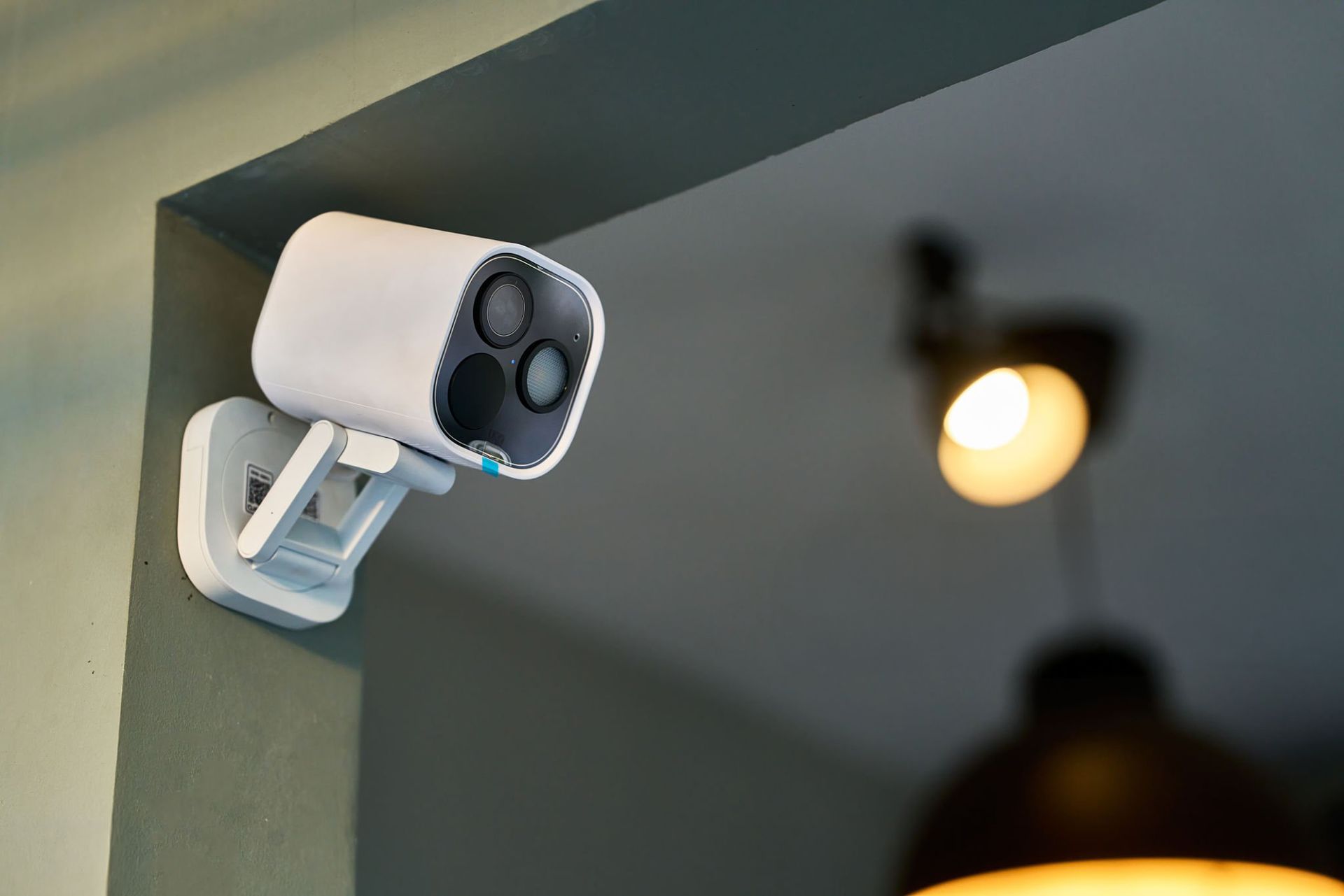 A wall-mounted security camera installed indoors near a light fixture.