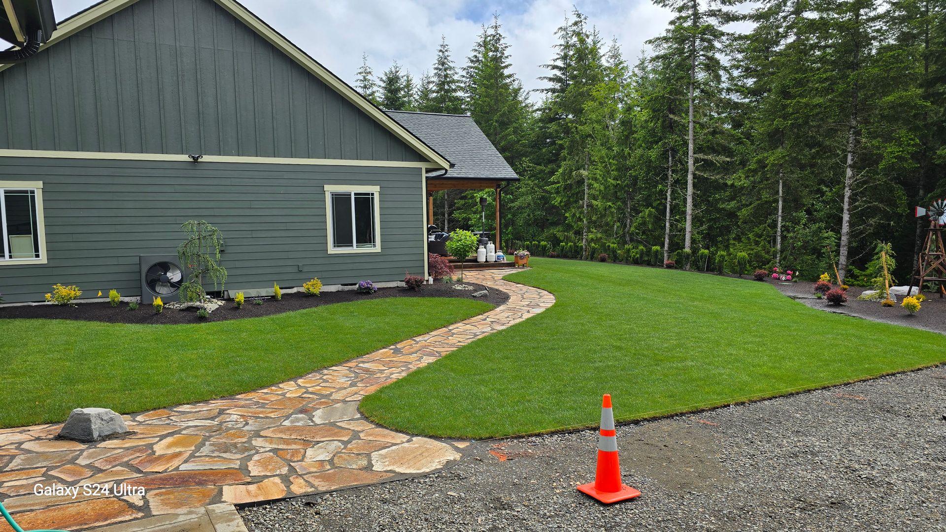 A house with a stone walkway leading to it is surrounded by grass and trees.