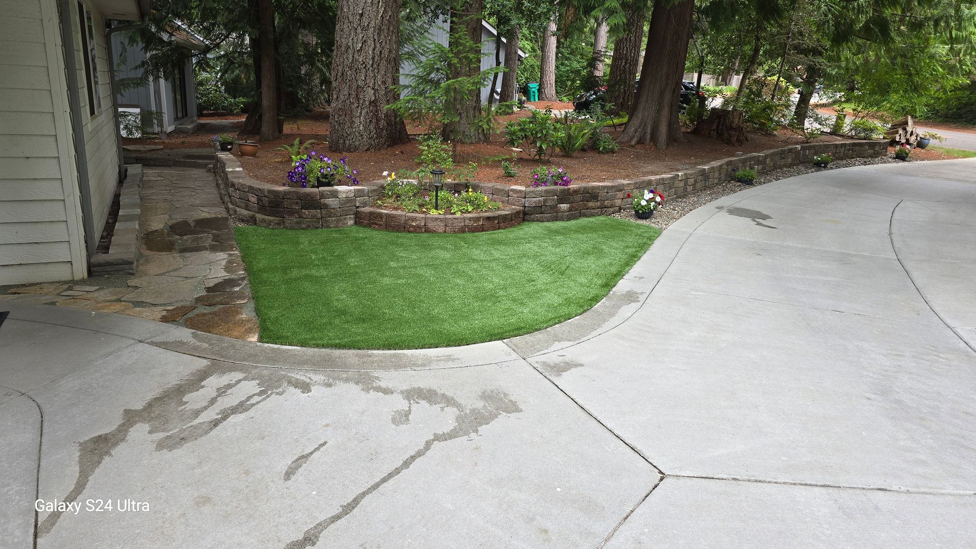 A concrete driveway leading to a house with a lush green lawn.