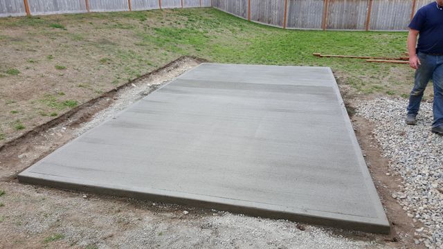 A man is standing on a concrete slab in a backyard.