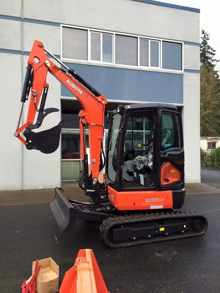 An orange kubota excavator is parked in front of a building
