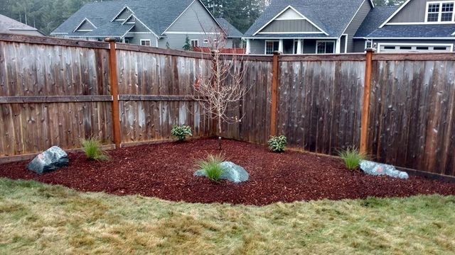 A wooden fence surrounds a garden with rocks and mulch.