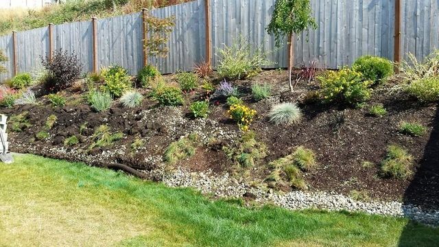 A wooden fence surrounds a hillside filled with lots of plants and flowers.