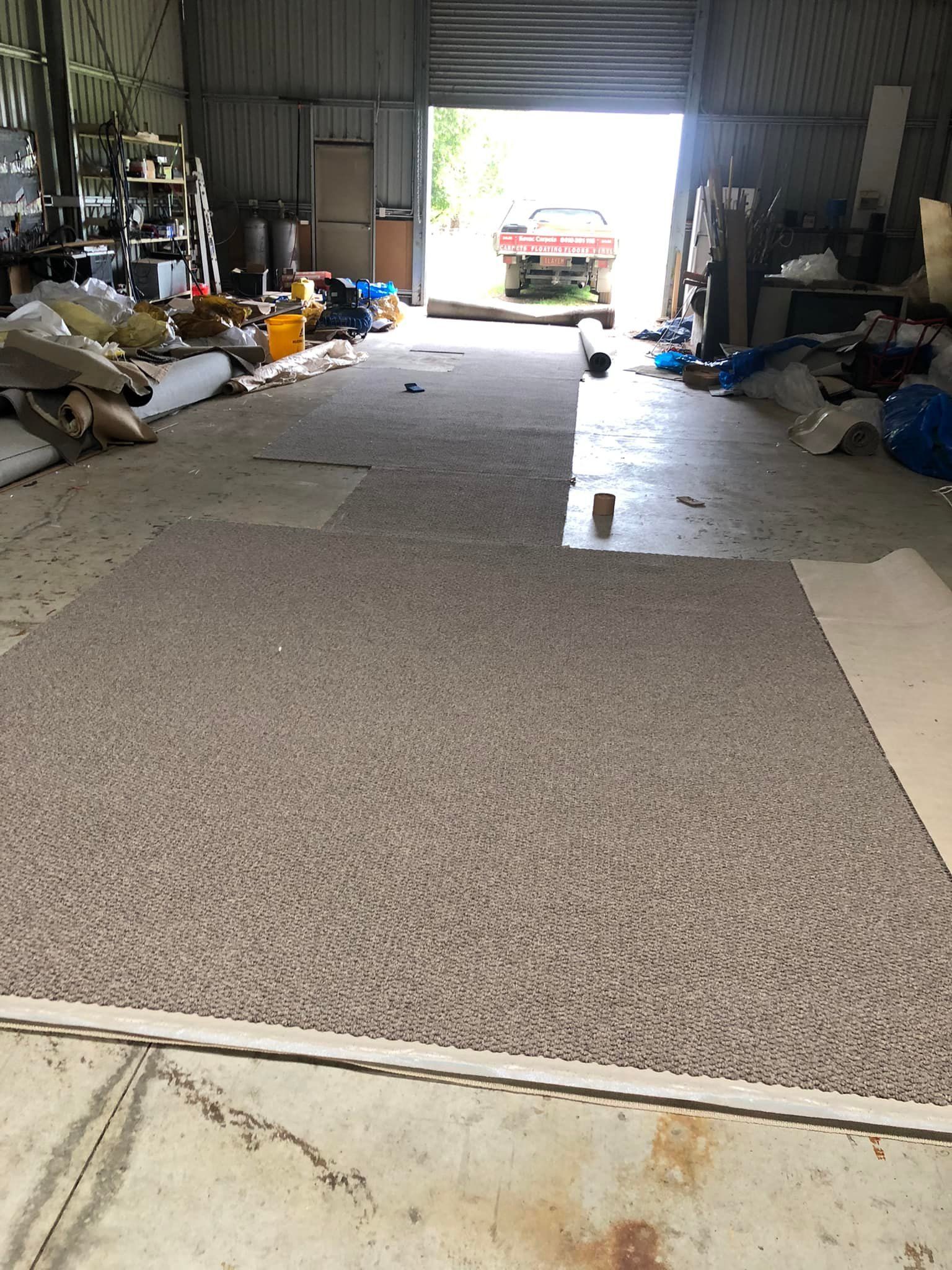 A large carpeted floor in a garage with a car parked in the background.