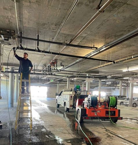 A man on a ladder is working on a pipe in a parking garage