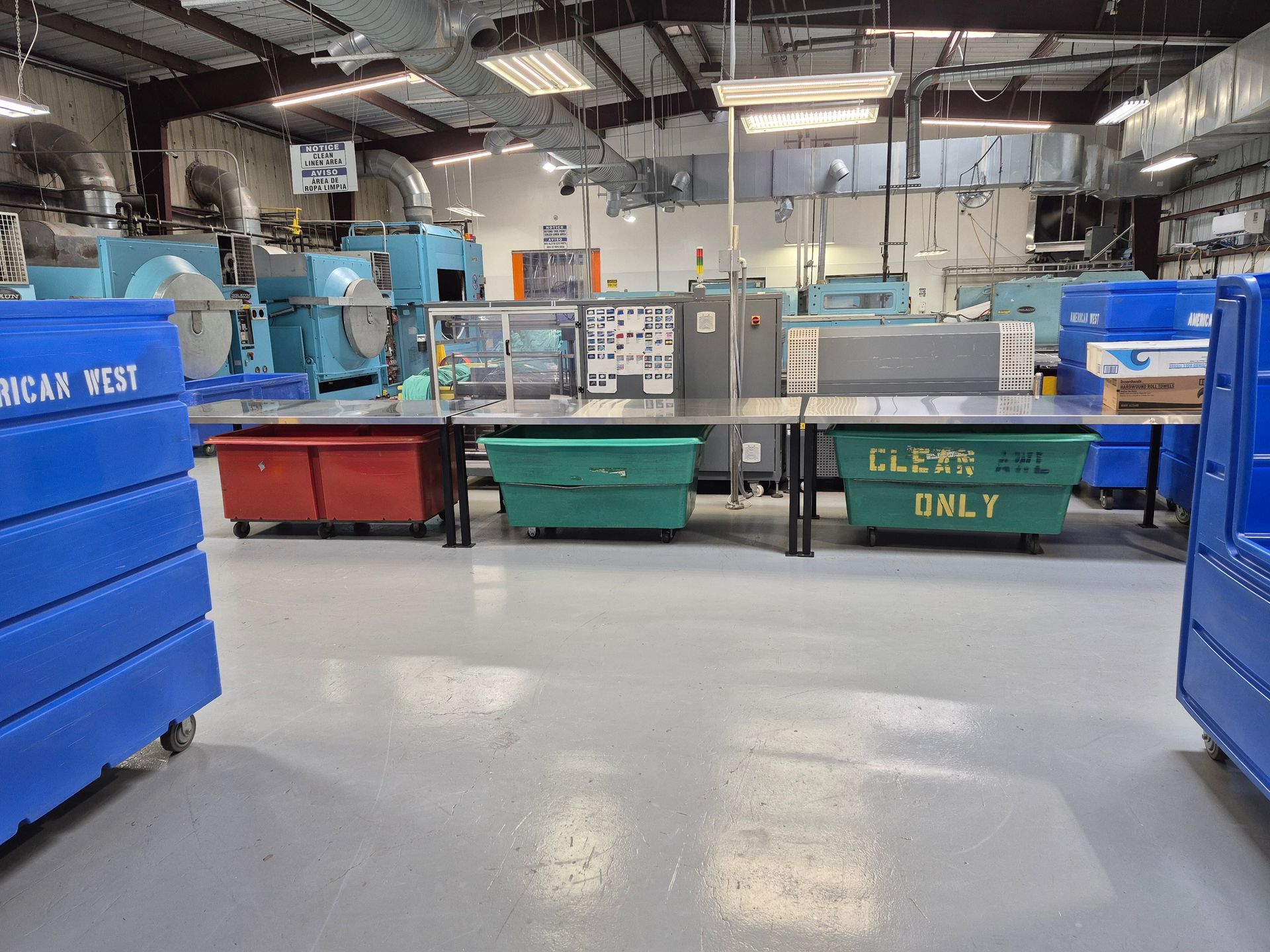 An industrial workspace with blue bins, equipment, and a large metal table.