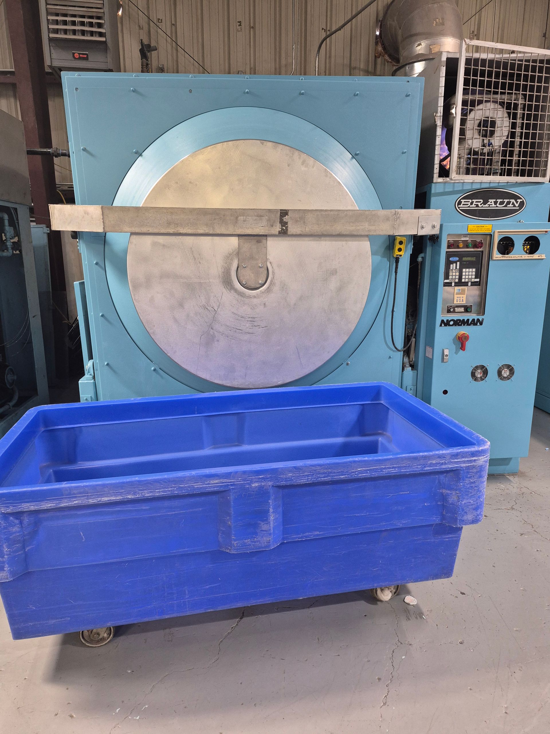 Blue industrial washing machine with a blue bin in front.