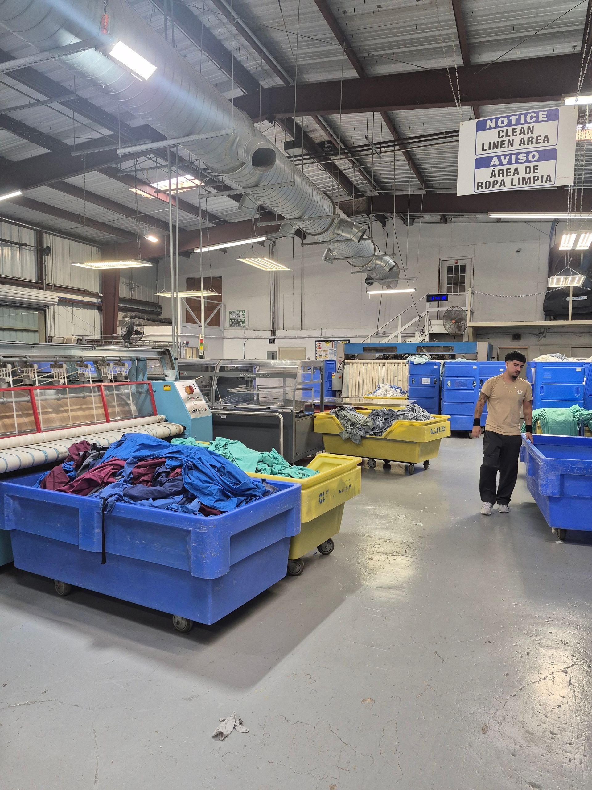 Laundry room with blue and yellow bins, machinery, and a person walking.