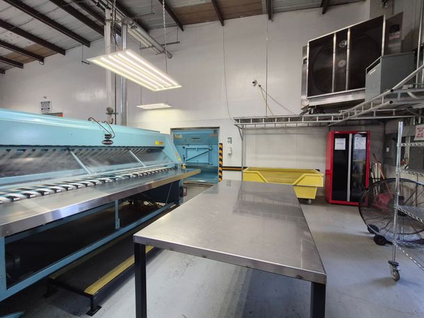Two yellow bins of laundry in front of a large commercial ironing machine.