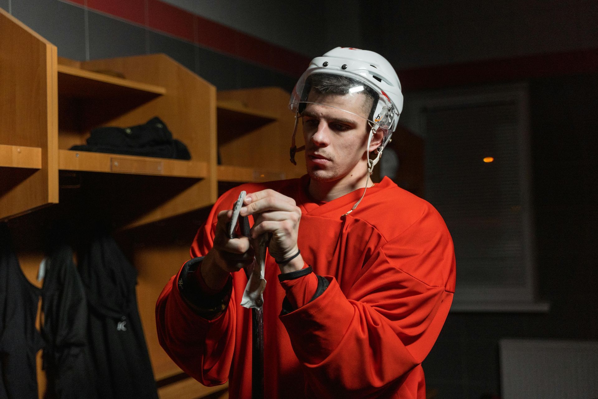 Hockey player in a red jersey and helmet in a locker room, holding a card.