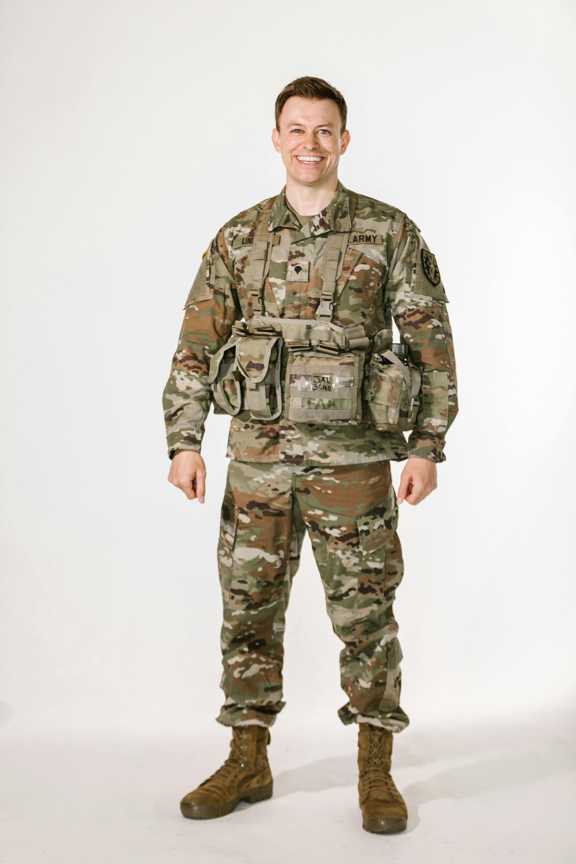 Smiling soldier in camouflage uniform, standing against a white background.
