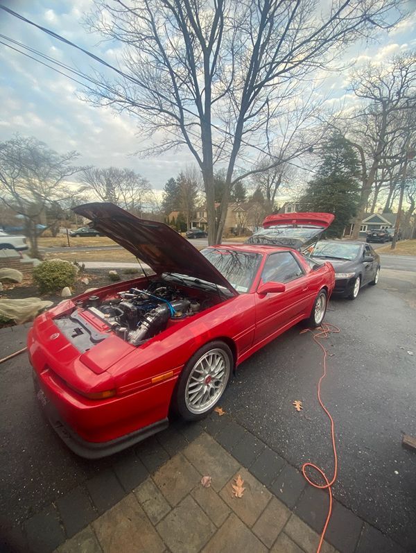 A red sports car with the hood up is parked in a driveway.