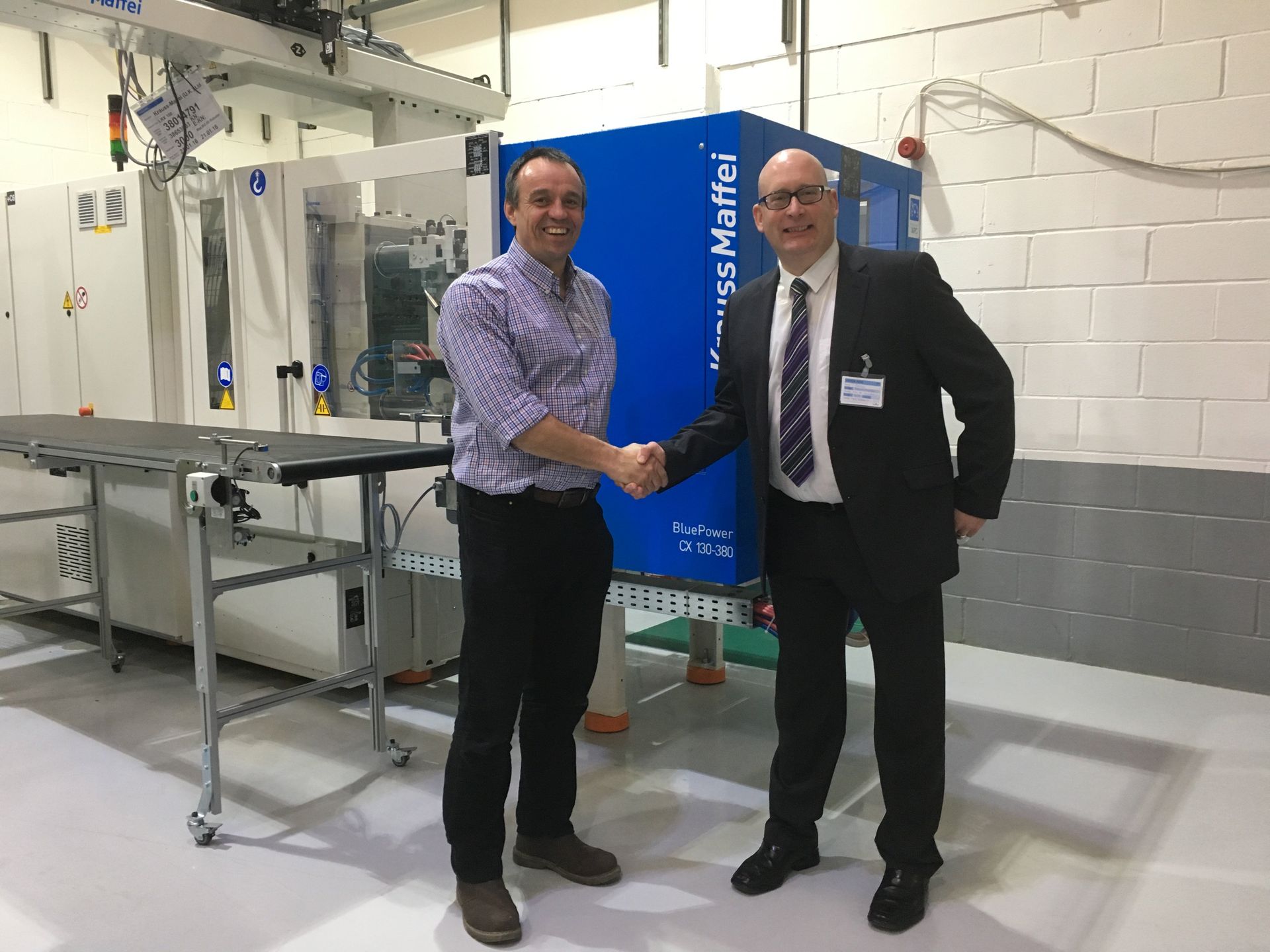 Two men are shaking hands in front of a machine.