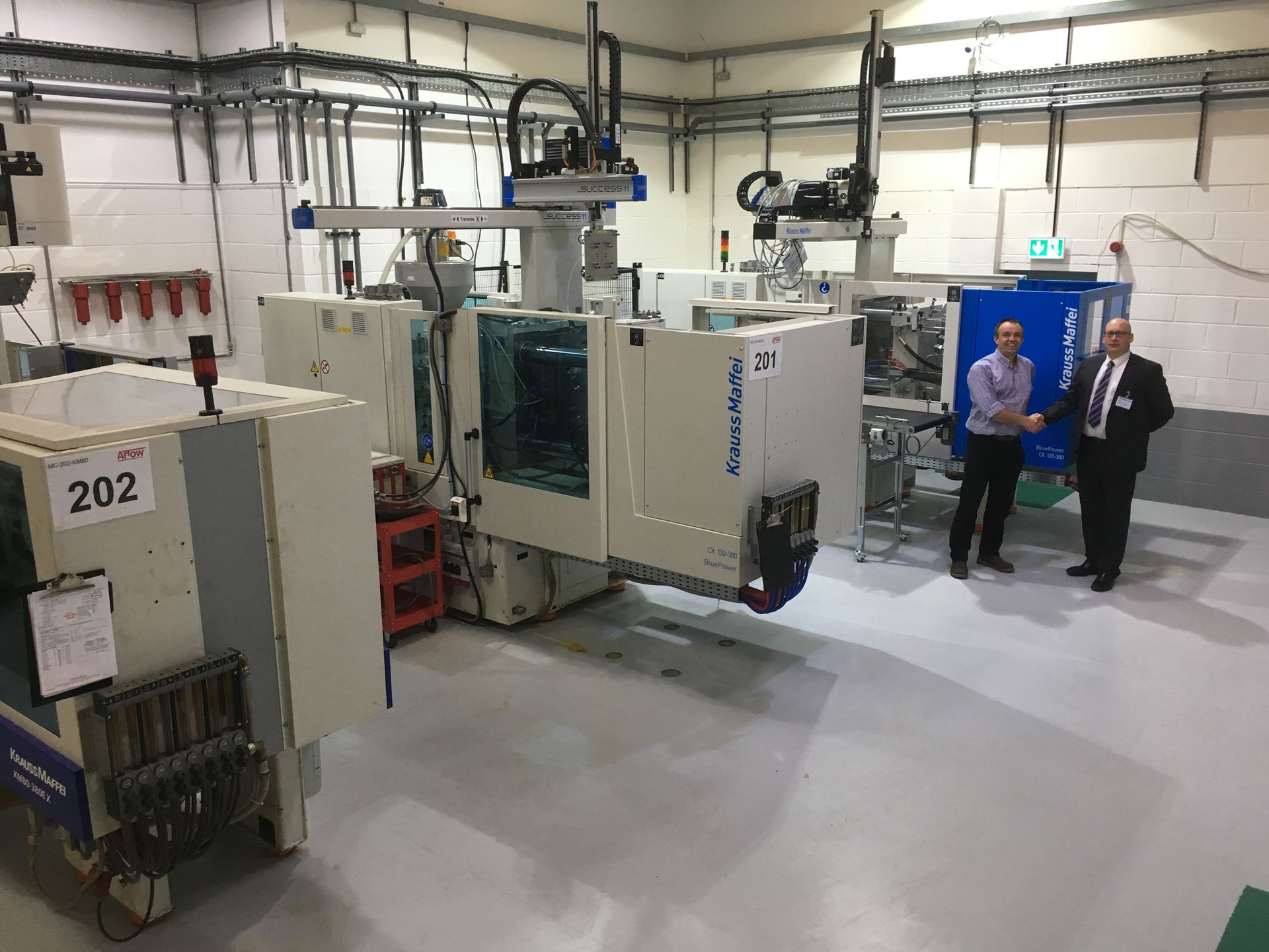Two men are standing in front of a machine in a factory.