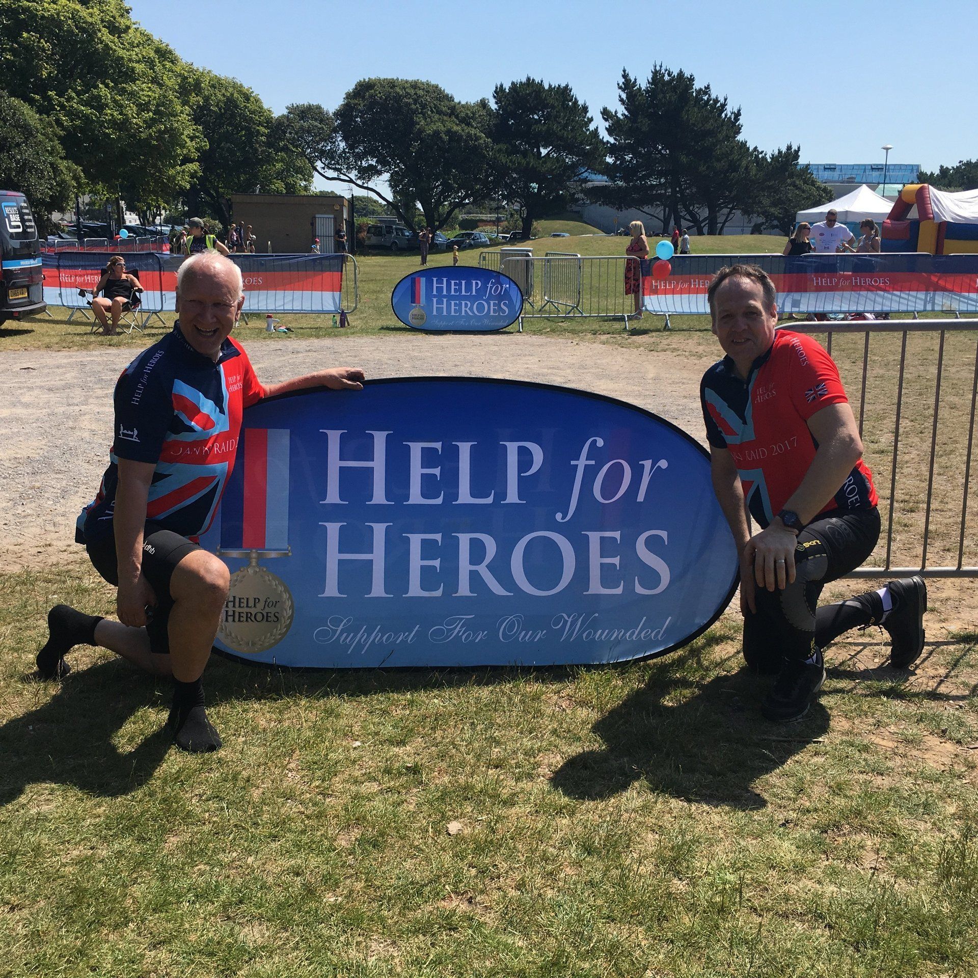 Two men kneeling in front of a help for heroes sign