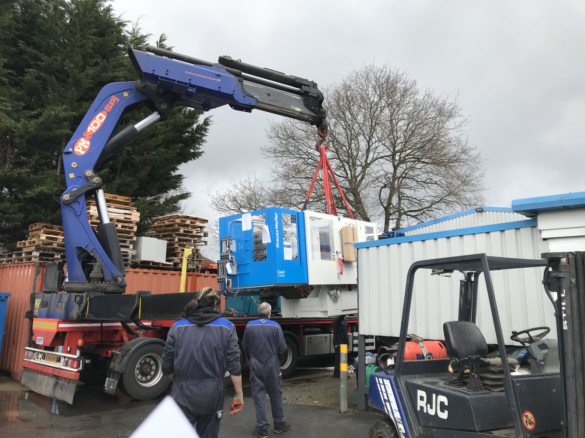 A crane is lifting a machine in a parking lot.