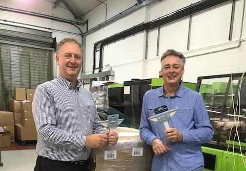 Two men are standing next to each other in a warehouse holding trophies.